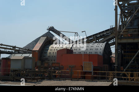 Eine Kugelmühle in einer Kupfer-Aufbereitung-Anlage mit einem großen kegelförmigen Vorrat im Hintergrund. Stockfoto