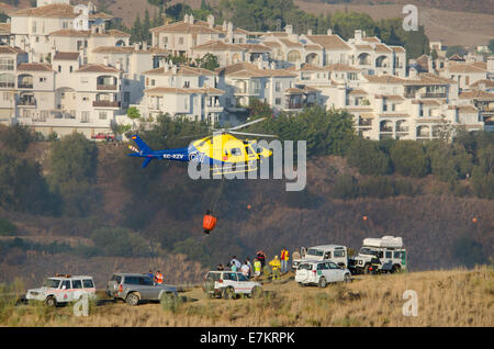 Aerial Feuerwehr mit Hubschrauber Wasser Bombardierung ein Buschfeuer in der Nähe eine Urbanisierung von Fuengirola, Andalusien, Spanien. Stockfoto