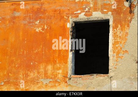 Leere Fensterrahmen bilden ein rechteckigen schwarzen Loch in ein orange Terrakotta bemalten Wand zeigen Verfall in Maribor, Slowenien Stockfoto