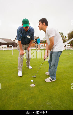 Von einem freiwilligen Golflehrer angewiesen, versucht blinder Hispanic Teenager einen Putt auf ein Golfkurs für blinde bei einem Kurs in Seal Beach, Kalifornien. Stockfoto