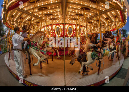 Hispanische Eltern Riemen ihre Kinder auf merry Go rund um mechanische Ponys für Sicherheit im Orange County Fair in Costa Mesa, CA. Stockfoto