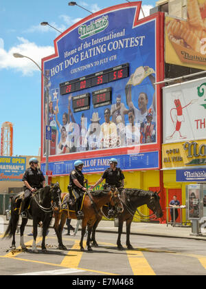 Helm tragen berittene Polizei auf Coney Island, New York City. Beachten Sie Werbeschild für das Hotdog-Wettessen in Nathans Restaurant, eine der Hauptattraktionen in diesem Vergnügungspark. Stockfoto