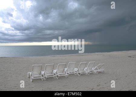 Einige Strandkörbe an einem leeren Strand mit einem dramatischen Himmel über dem Ozean Stockfoto