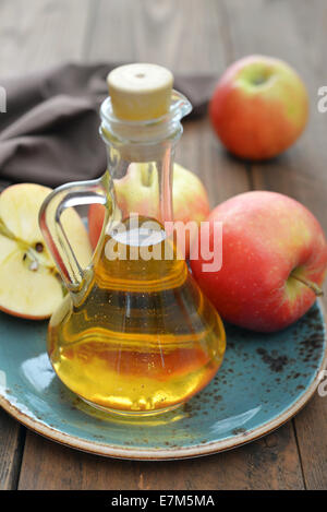 Apfelessig in Glasflasche und frische Äpfel auf hölzernen Hintergrund Stockfoto