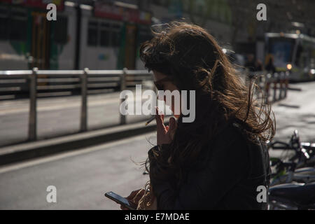 Junge Frau Rauchen beim Blick auf ihr Handy Stockfoto