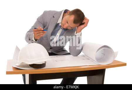 Architekt, zur Lösung eines Problems auf einen Bauplan sitzen an einem kleinen Holztisch mit seinem Kopf auf seine Hand und Stift an der anderen, isoliert auf weiss. Stockfoto