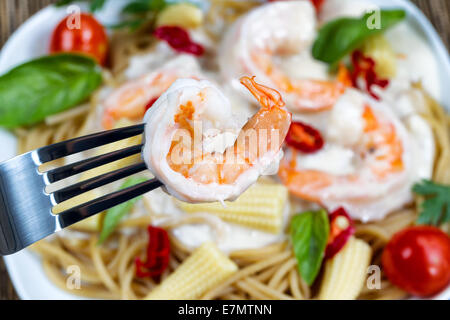 Makro-Ansicht von Edelstahl Gabel halten einzelne Garnelen mit Alfredo Pasta-Essen auf weiße Platte im Hintergrund gelegt Stockfoto