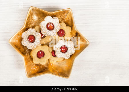 einen goldenen Becher, geformt wie ein Star. gefüllt mit Weihnachtsgebäck auf weißem Holz Hintergrund Stockfoto