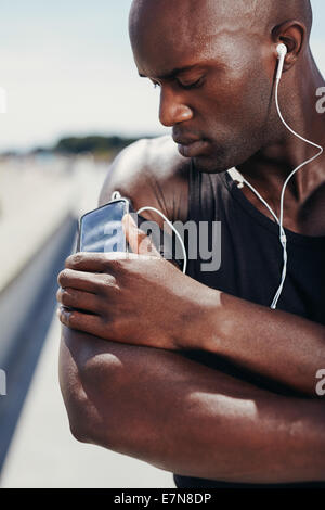 Afrikanische muskulöse Athleten Musik hören. Männliches Model Musikhören von seinem Handy auf Armbinde. Stockfoto