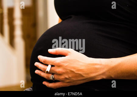 Schwangere Frau hält eine Zigarette Stockfoto