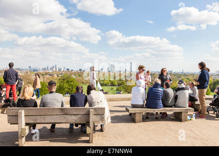 London Aussichtspunkt. Leute sitzen auf Bänken in der Frühlingssonne die entfernte Skyline der Stadt von Primrose Hill, London, England, Großbritannien Stockfoto