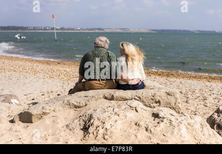 Älteres paar Mann und Frau sitzen auf dem Sand, Blick auf das Meer über die Bucht von Christchurch in Mudeford Stockfoto