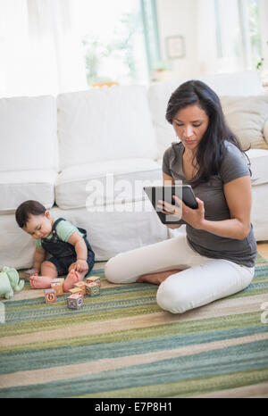 Mutter mit tablet-pc, während ihr Sohn (6-11 Monate) spielen mit Bausteinen Stockfoto