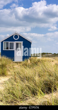 Blaue Strandhütte in Mudeford Dorset mit Strandhütten auf einem grasbewachsenen Sandstrand mit blauem Himmel und weißen Wolken Stockfoto