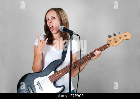 Mädchen mit Gitarre und Mikrofon auf grauem Hintergrund isoliert Stockfoto