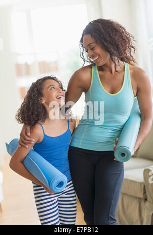 Mutter und Tochter (8-9) Holding Yoga Matten im Wohnzimmer Stockfoto