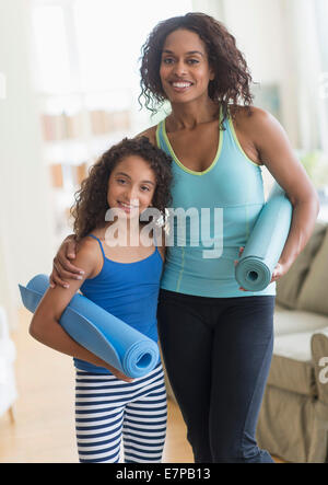 Mutter und Tochter (8-9) Holding Yoga Matten im Wohnzimmer Stockfoto