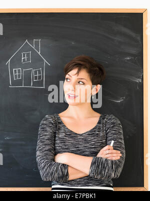 Frau vor Tafel mit Haus-Zeichnung Stockfoto