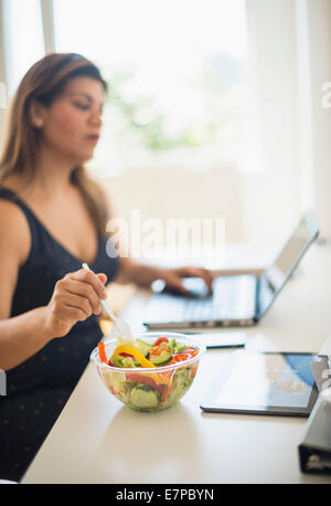 Frau Salat essen und mit Laptop im Büro Stockfoto