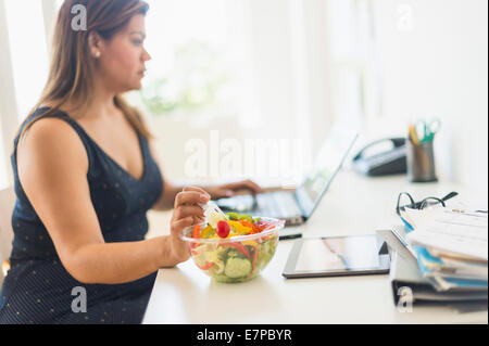 Frau Salat essen und mit Laptop im Büro Stockfoto