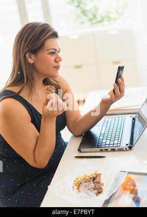 Frau Croissant Essen und mit Handy im Büro Stockfoto