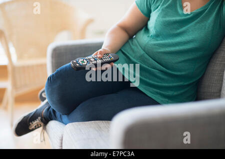 Frau sitzt auf dem Sofa mit Fernbedienung Stockfoto