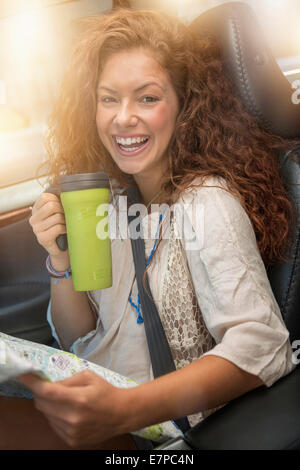 Frau sitzt im Auto mit Karte und Einweg-cup Stockfoto