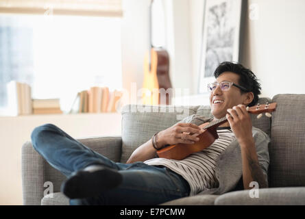 Mann auf Sofa sitzen und spielen der ukulele Stockfoto