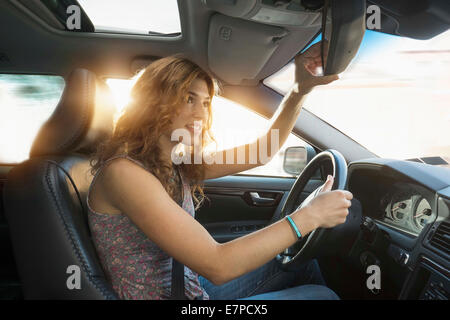 Junge Frau, die Spiegel der hinteren Ansicht während der Fahrt einstellen Stockfoto