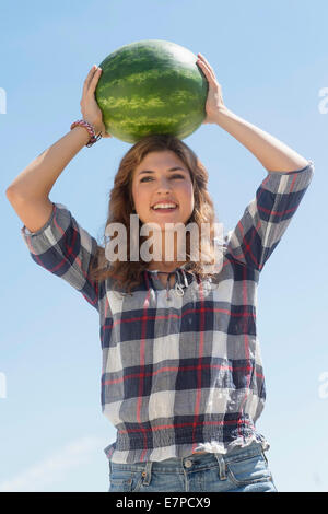 Junge Frau, die am Kopf Wassermelone Stockfoto