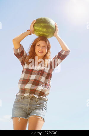 Junge Frau, die am Kopf Wassermelone Stockfoto