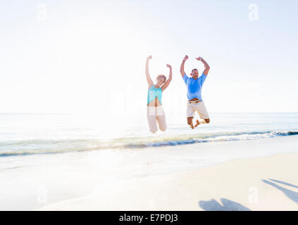 Älteres Paar mit erhobenen Armen im Meer springen Stockfoto