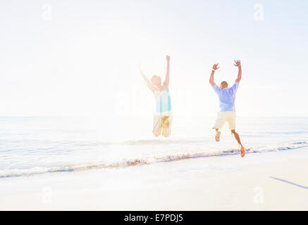 Älteres Paar mit erhobenen Armen im Meer springen Stockfoto