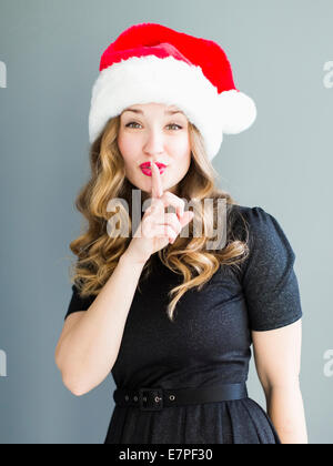 Studio-Porträt der Frau trägt Weihnachtsmütze mit Finger auf Lippen Stockfoto