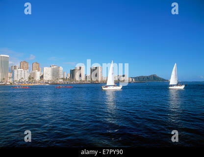 Ausleger-Kanus und Segelboote verlassen Ala Wai Hafen mit Diamond Head und Waikiki Hotels von Magic Island gesehen Stockfoto