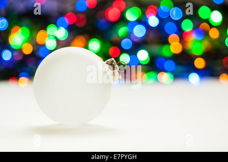 Ein einsamer weißer Christbaumschmuck wird gegen einen mehrfarbigen Bokeh festgelegt. Auch als Hintergrund oder in Weihnachtskarten einsetzbar. Stockfoto