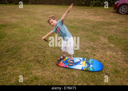 Fünf Jahre alter Junge spielt auf einem Surfbrett auf Karrageen Campingplatz Bolberry, in der Nähe von Hope Cove, South Devon, England, Vereinigtes Königreich. Stockfoto