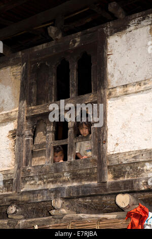 Ost Bhutan, Trashi Yangtse, Kinder durch traditionellen hölzernen Bauernhaus Fenster Stockfoto