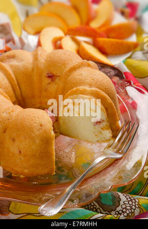 Schließen Sie herauf Studio Bild von einem Pfirsich Sandkuchen mit sanfter Beleuchtung. Ein Teller mit in Scheiben geschnittenen Pfirsiche ist im Hintergrund unscharf. Stockfoto