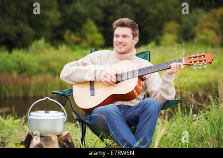 lächelnder Mann mit Gitarre und Dixie im camping Stockfoto