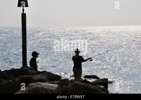 Silhouette eines Paares, das von einem Felsvorsprung aus im Meer fischt. Stockfoto