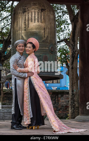 Bräutigam in grau, rosa Ao Dai Braut mit Bronzeglocke Hintergrund. Stockfoto