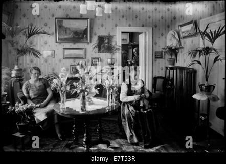 Ein Foto aus dem Jahr 1910-1930, das zwei Frauen in einem Haus in Reykjavik zeigt, mit Blumen im Inneren. Das Bild zeigt ein gemütliches Wohnzimmer mit Strickarbeiten, das isländische Hausleben während des frühen 20. Jahrhunderts veranschaulicht. Stockfoto