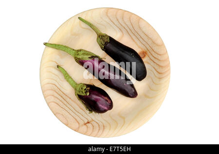 drei Auberginen auf einer runden handgemachte hölzerne Platte Stockfoto