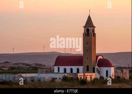 Einer griechischen Kirche im Vordergrund während einer Windfarm mit Anlagen in der Ferne nutzt den Wind um alternative Energie zu erzeugen Stockfoto