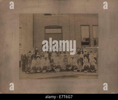 Ein Vintage-Foto einer Schulklasse, wahrscheinlich aus dem frühen bis Mitte des 20. Jahrhunderts. Das Bild zeigt eine Gruppe von Schülern, die vor ihrer Schule posieren, wobei der Lehrer in der Gruppe sichtbar ist. Das Schwarzweiß-Foto bietet einen Einblick in das Schulleben dieser Zeit. Stockfoto