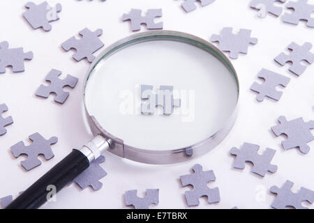 Hand hält klassisch Lupe und Suche Führer Puzzleteil unter anderem auf weiß. Stockfoto