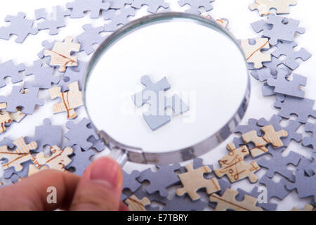 Hand hält klassisch Lupe und untersuchen einzelne kleine Puzzleteil unter anderem auf weiß. Stockfoto