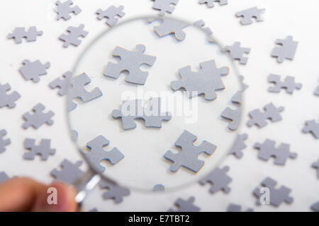 Hand mit klassischen Stil Lupe und kleine Puzzleteile auf weiß. Stockfoto