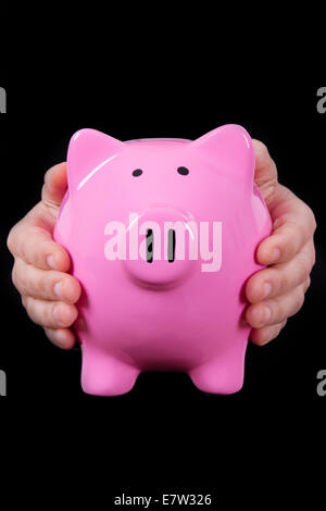 Rosa Piggy Bank-holding von zwei Händen, isoliert auf schwarz. Stockfoto